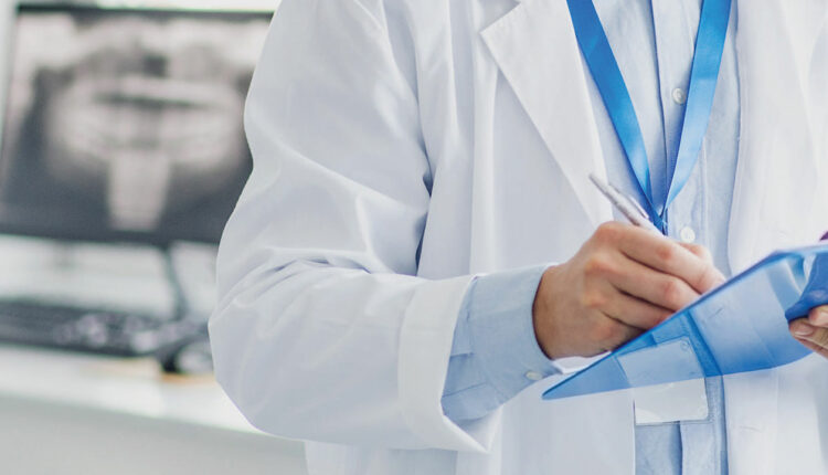 Male dentist writing on a clip board, reviewing surgical checklist.