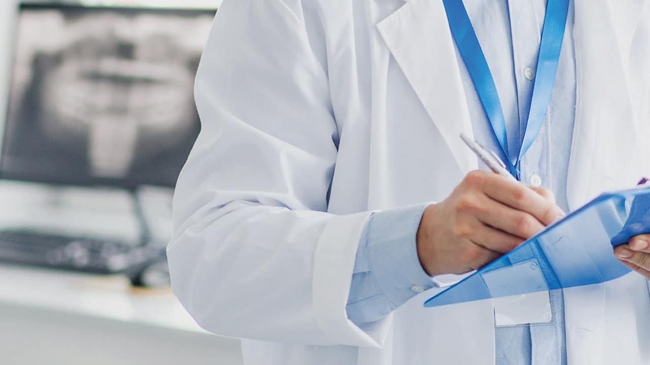 Male dentist writing on a clip board, reviewing surgical checklist.
