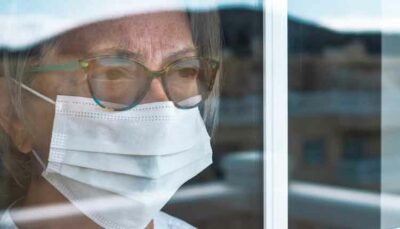 elderly woman with a mask looking out of the window