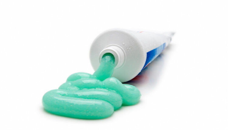Turquoise toothpaste flowing from an open tube on a white surface