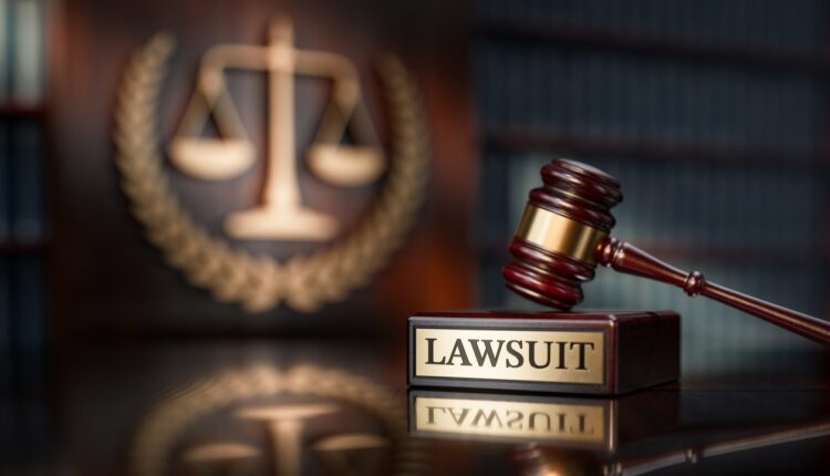 Judge’s gavel above a wooden stand labeled “Lawsuit,” with scales of justice in the background
