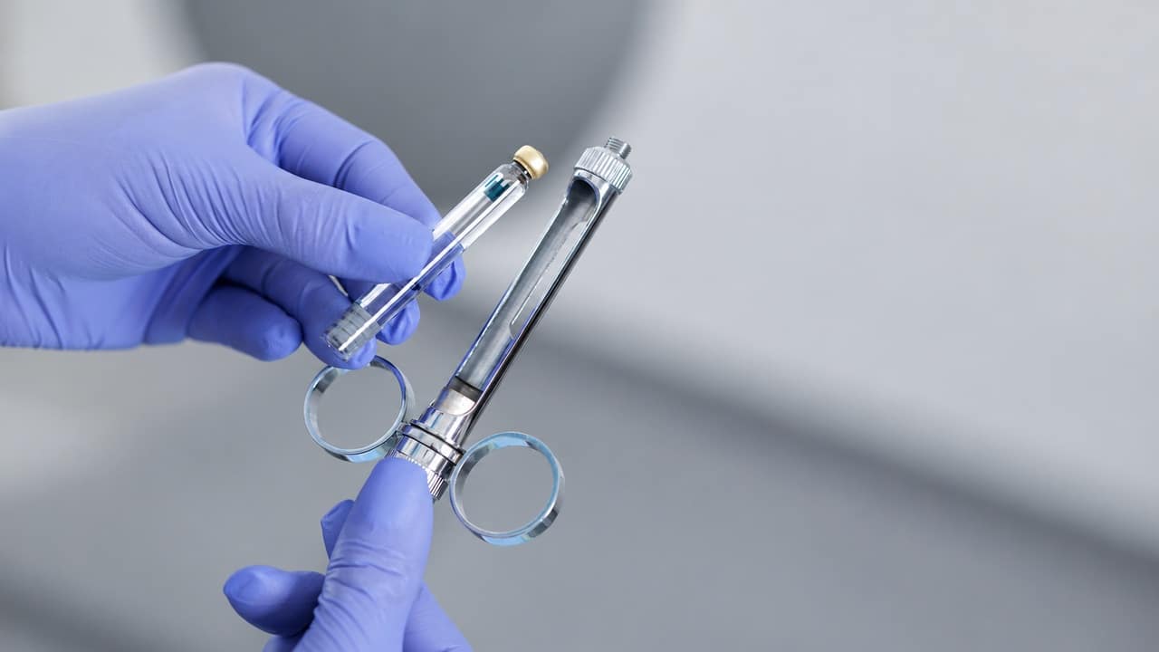 Gloved hands holding a dental anesthetic cartridge and metal aspirating syringe