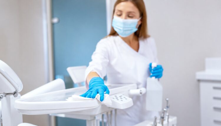 Masked dental worker wearing blue gloves disinfecting a dental chair surface